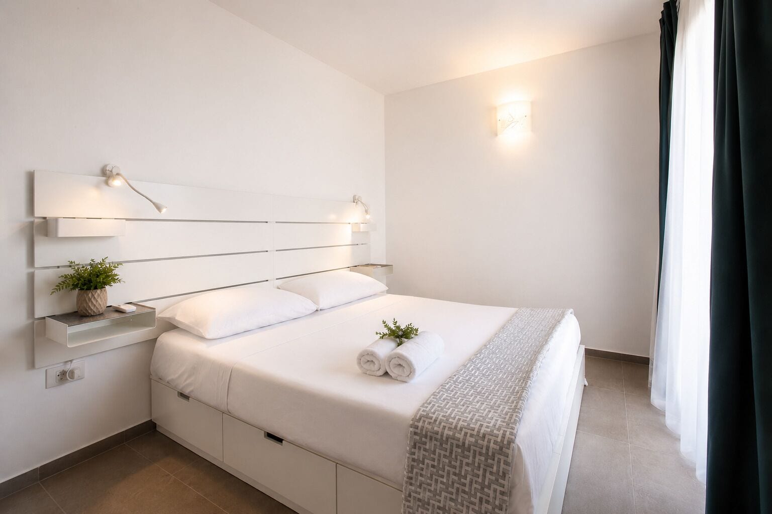 Ein modernes Schlafzimmer mit Bett, Nachttischen, einer Wandleuchte und einem Fenster mit Vorhängen.