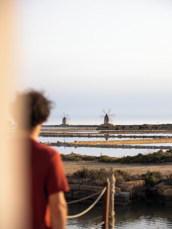 A person in a red shirt standing by a body of water with windmills in the background.