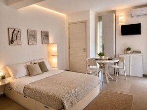 A modern bedroom with a bed, bedside tables, a desk, chairs, a TV, and artwork on the wall. - 18 Gradi Apartments (Marsala)