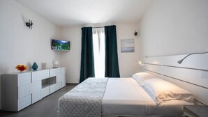 A modern bedroom with a bed, a TV, a dresser, and a window with curtains. - 18 Gradi Apartments (Marsala)