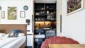 A compact hotel room with a bed, a small kitchenette, a red chair, and a dining table. - Design Apartment 'Fauna by Kamelu' with Private Terrace and Parking (Gengenbach)
