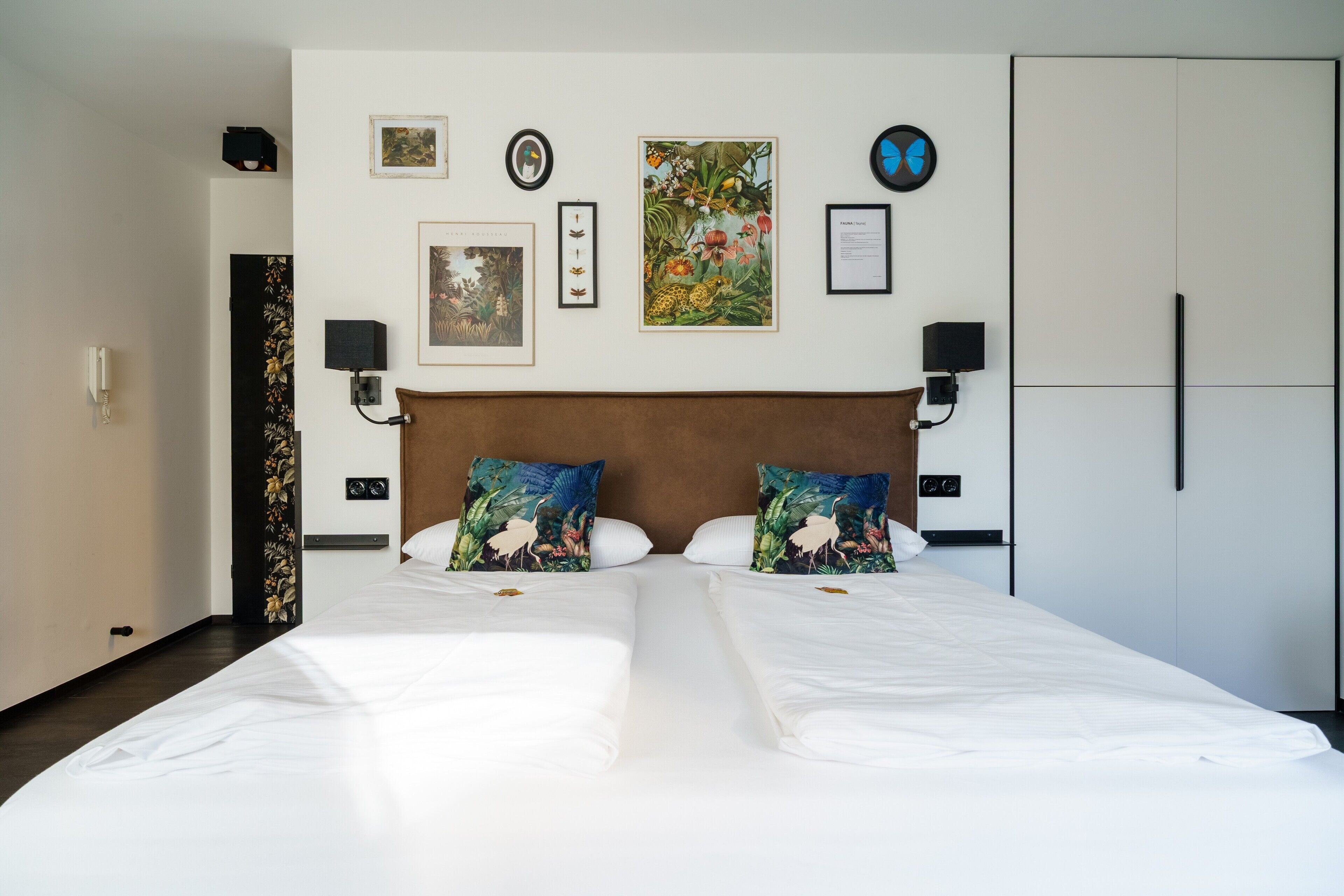 A double bed with white linens, two decorative pillows, a headboard, and wall-mounted artwork.