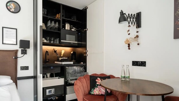 A compact kitchen with modern appliances, a dining area with a round table, and a red chair. - Design Apartment 'Fauna by Kamelu' with Private Terrace and Parking (Gengenbach)