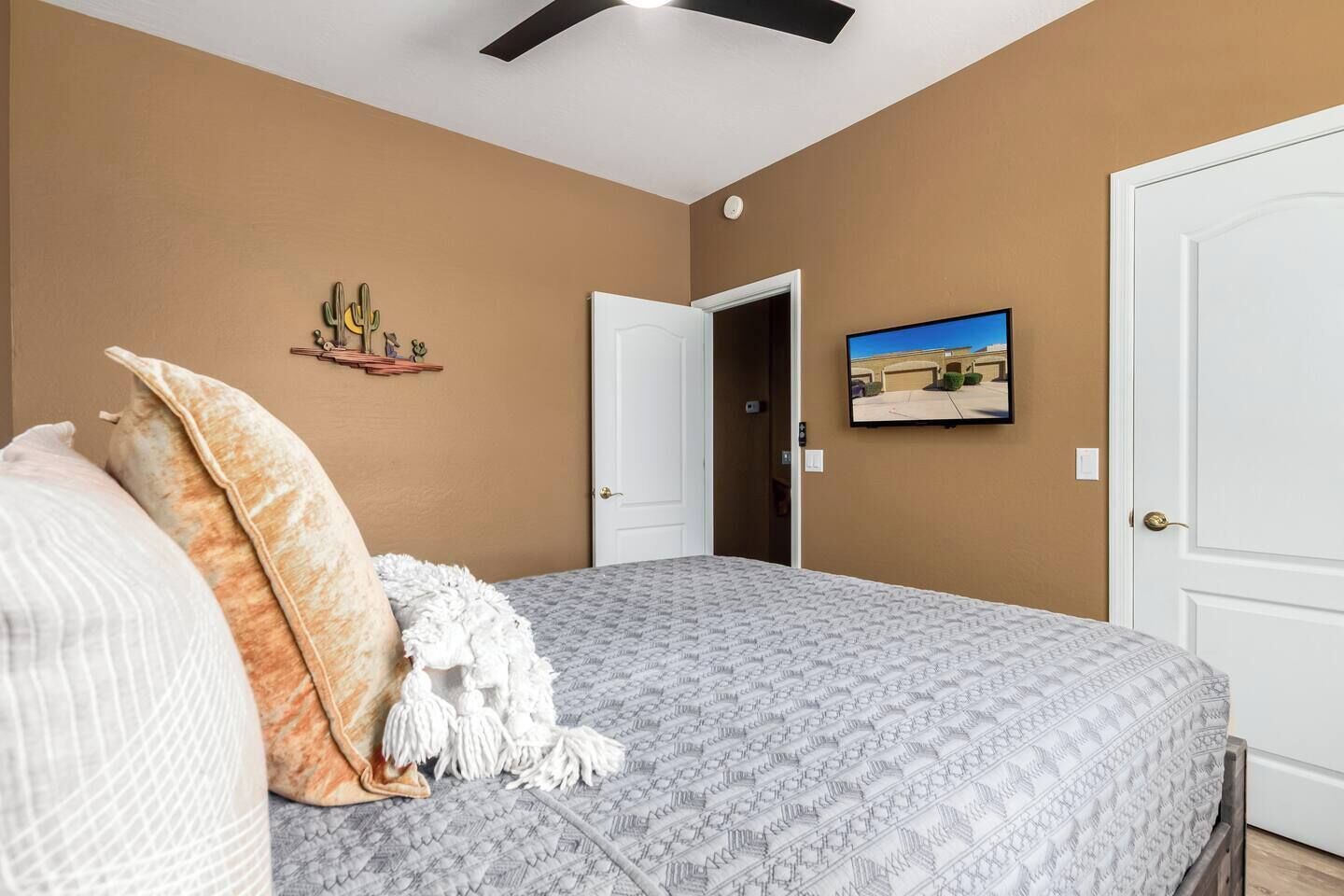 Een slaapkamer met een bed, kussens, een wandtelevisie en een deur naar een andere kamer.