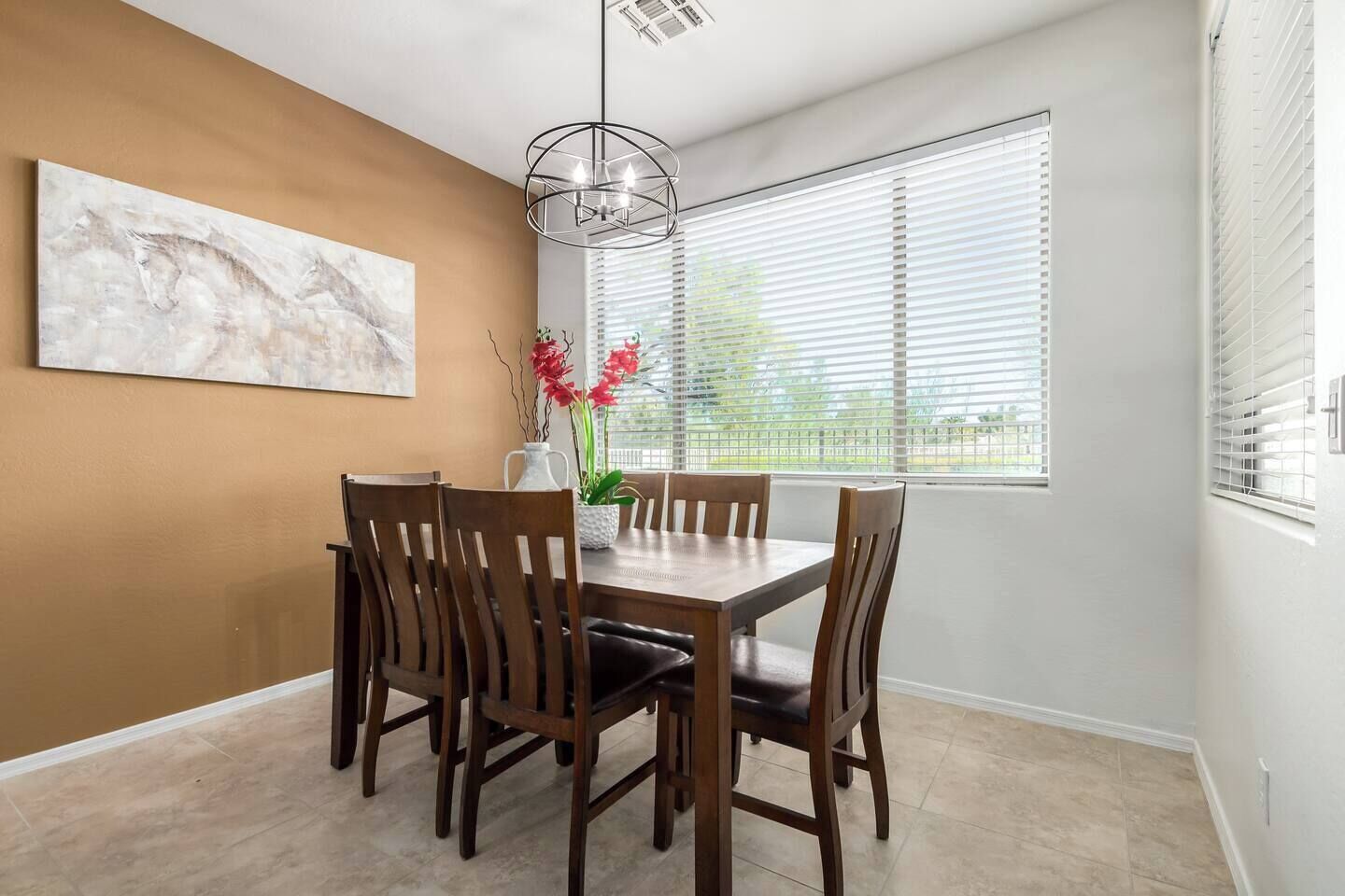 A dining area with a wooden table and chairs, a vase with flowers, and a painting on the wall.