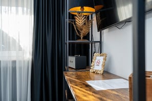 Ein Hotelzimmer mit einem Holztisch, einer Lampe mit Blattmuster, einem Rauchverbot-Schild und einem Fernseher an der Wand.