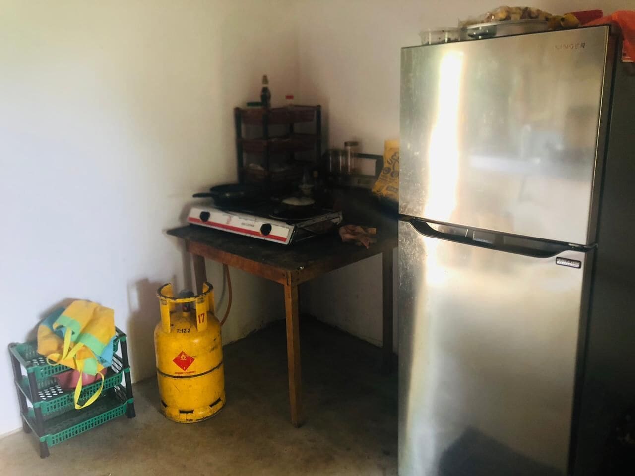 A compact kitchen with a stainless steel refrigerator, a gas stove, and a gas cylinder.