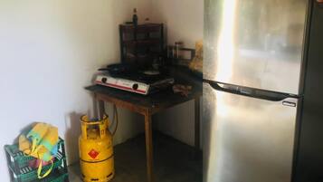 A compact kitchen with a stainless steel refrigerator, a gas stove, and a gas cylinder.