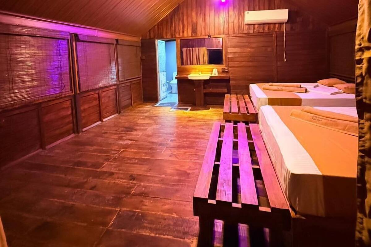 Une chambre aménagée dans les combles, avec des murs en bois et un plafond en pente. On y trouve un lit, un banc et un bureau avec une chaise.