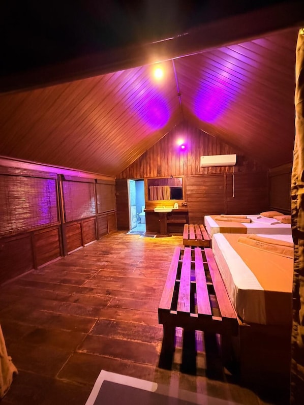 An attic bedroom with wooden walls and a sloped ceiling. There is a bed, a bench, and a desk with a chair. - Kolla Watersong Eco Cabana resort (Sigiriya)