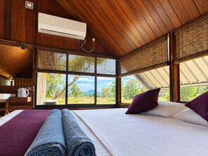 Une chambre dotée d’un grand lit, d’un plafond en bois, d’un appareil de climatisation et offrant une vue sur un paysage par la fenêtre.