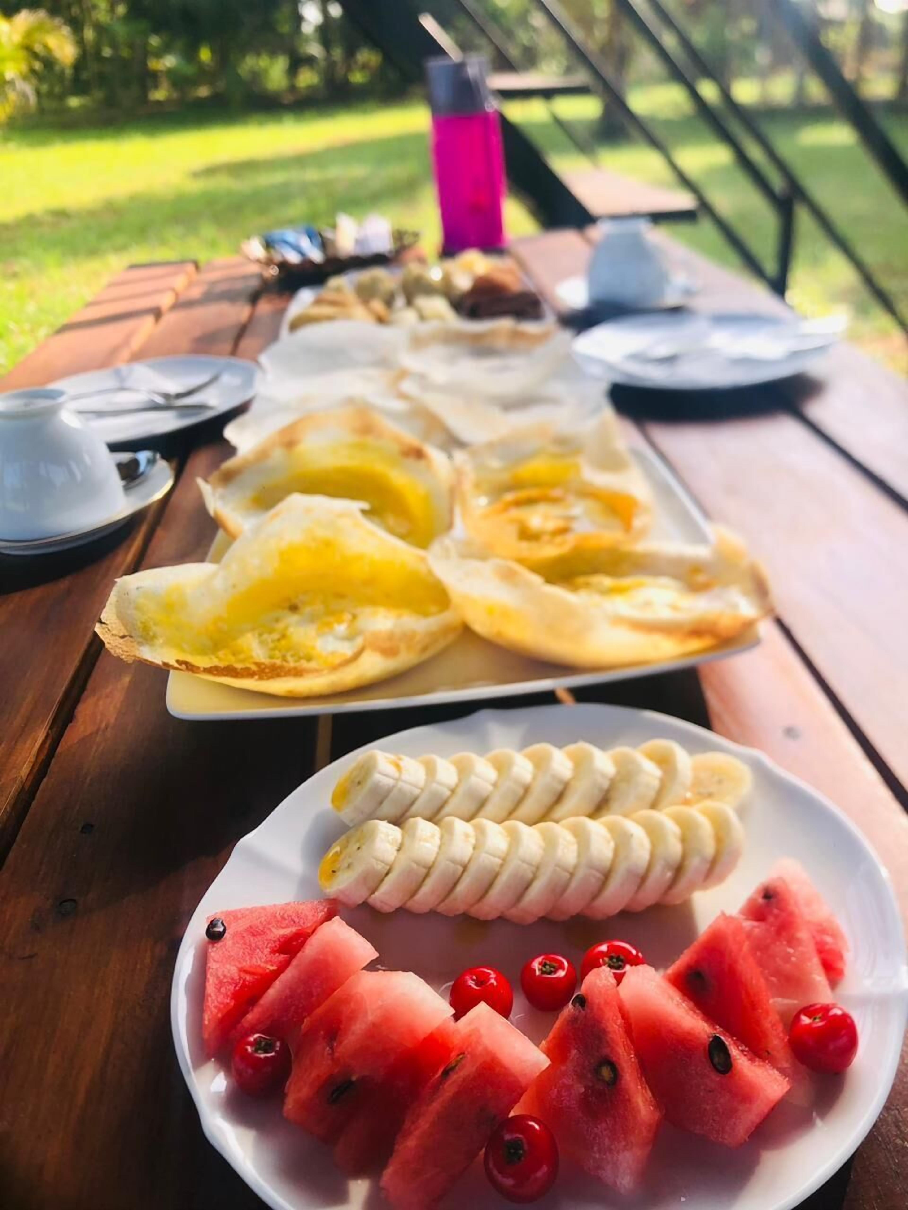 A picnic setup with a variety of foods including pancakes, bananas, and watermelon slices on a wooden table.