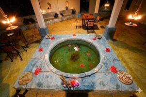 Una fuente de piedra con agua, rodeada por un pedestal de piedra con velas y flores.
