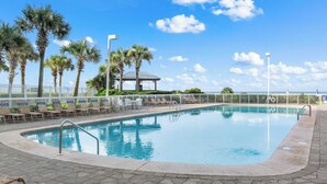 A pool area with lounge chairs and palm trees, a covered seating area, and a view of the ocean. - Seaside Beach & Racquet Club 1115 (Orange Beach)