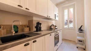 Eine kompakte Küche mit weißen Schränken, einem Spülbecken und einem kleinen Backofen. Ein Fenster lässt natürliches Licht herein und bietet einen Ausblick.