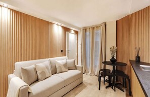 A modern living room with a beige sofa, a small round table with chairs, and a wooden panel wall. - A Refined Loft-Studio in Saint-Germain (Paris)