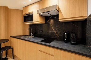 A modern kitchen with wooden cabinets, a built-in microwave, a stainless steel range hood, a black countertop, a sink, and a coffee maker. - A Refined Loft-Studio in Saint-Germain (Paris)