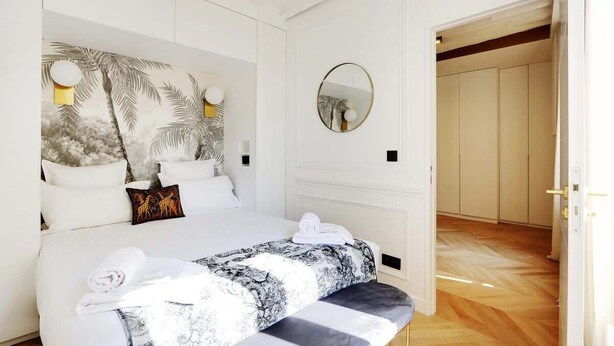 Une chambre à coucher comprenant un lit, une table de chevet, un miroir et une porte donnant sur une autre pièce.