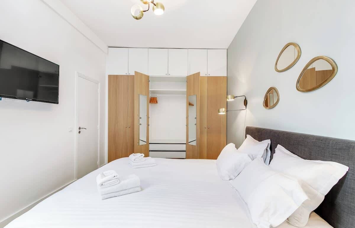 Moderni hotellihuone, jossa on suuri sänky, seinälle asennettu televisio ja erillinen vaatehuone, jossa on puuovet.