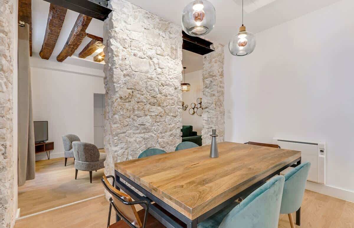 A dining area with a rustic stone wall, wooden table, and modern chairs.