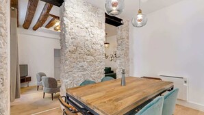 A dining area with a rustic stone wall, wooden table, and modern chairs. - An Exceptional 2-BR/2BA in Le Marais (Paris)