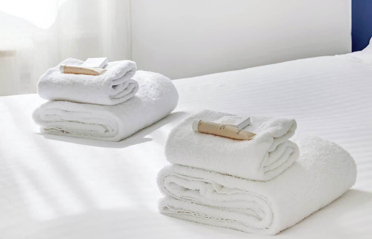 Una cama bien hecha con sábanas blancas y dos toallas enrolladas con pinzas de madera a un lado.
