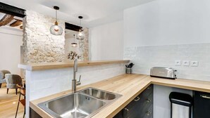 A modern kitchen with a stone accent wall, a wooden countertop, a stainless steel sink, and a toaster. - An Exceptional 2-BR/2BA in Le Marais (Paris)