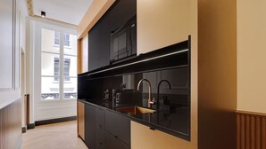 Een moderne keuken met zwarte kastjes, een roestvrijstalen spoelbak en een raam met uitzicht op een gebouw.