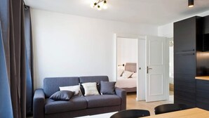 Una sala de estar moderna con un sofá gris, una mesa de comedor de madera y una cocina negra con horno empotrado.