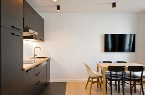 A modern kitchen with dark cabinetry, a wooden countertop, and a built-in stove. There is a dining area with a table and chairs, and a flat-screen TV mounted on the wall. - A Pleasant 2-BR near Nation and Charonne (Paris)