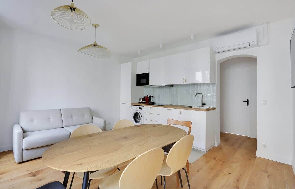 Een moderne keuken met witte kasten, een houten eettafel en een grijze bank.