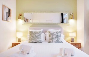 Een hotelkamer met een groot bed, twee nachtkastjes, een spiegel en een lijst met een afbeelding aan de muur.