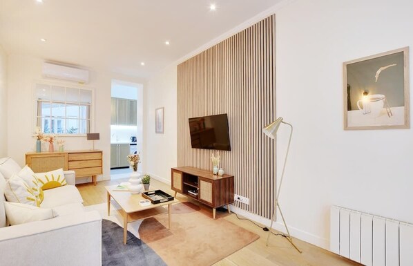 Een moderne woonkamer met een bank, salontafel, televisie en een wand van houten panelen.