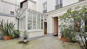A courtyard with potted plants, a glass door, and a brick floor. - An Amazing 2-BR in Le Marais (Paris)