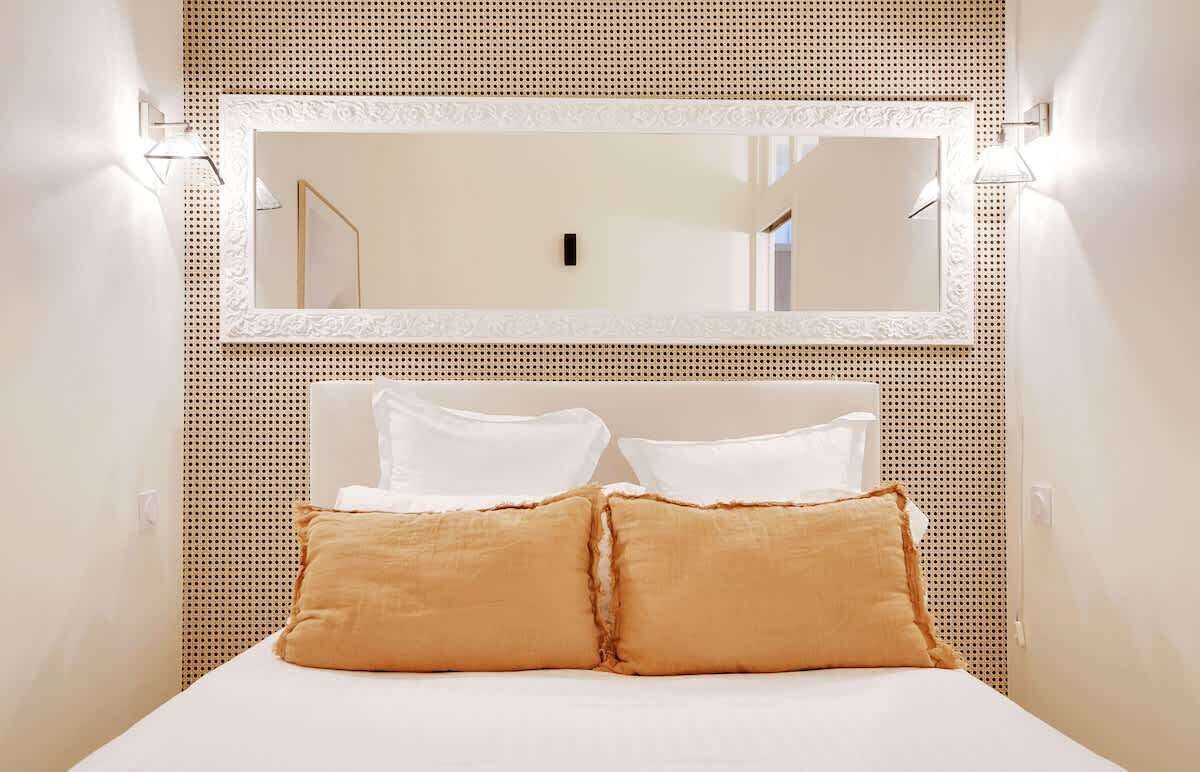 A hotel room with a large bed, white bedding, a decorative mirror, and a textured wall.