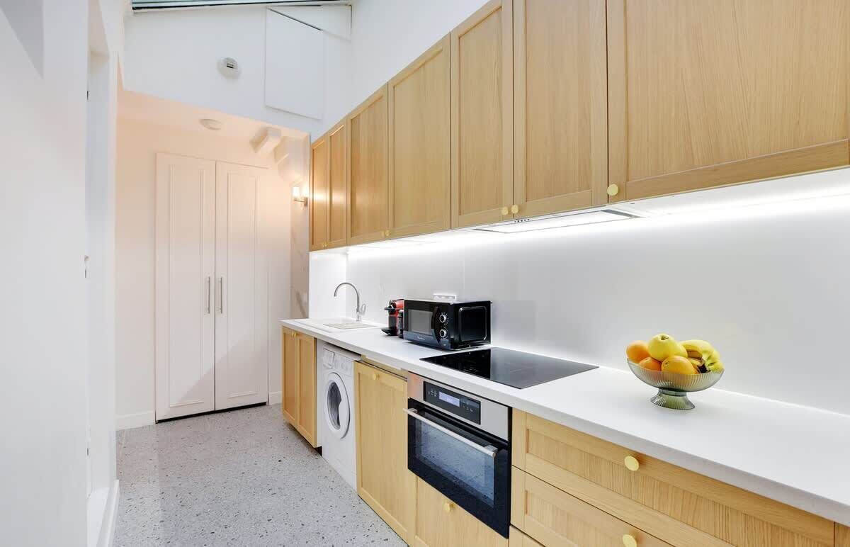 A modern kitchen with wooden cabinets, a washing machine, an oven, and a microwave.