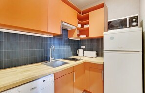 Eine Küche mit orangenen Schränken, einem weißen Kühlschrank und einer blauen gefliesten Spritzschutzwand.