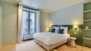 Un dormitorio con una cama grande, una mesita de noche, un radiador y una ventana con cortinas.