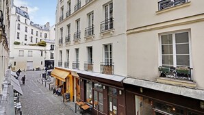 En smal gata med byggnader på båda sidor, där det finns ett café med uteservering och en butik som syns tydligt med en skylt.
