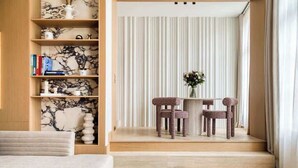 A modern living room with a sofa, a wooden bookshelf, a marble-patterned wall, a striped curtain, and a small table with two chairs. - Oniri - 1-BR with Services - Grand Augustin 1 (Paris)