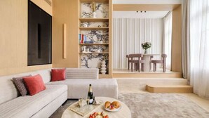 A modern living room with a sofa, coffee table with snacks, a bookshelf, and a dining area with chairs. - Oniri - 1-BR with Services - Grand Augustin 1 (Paris)