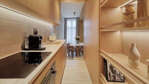 A narrow, modern kitchen with wooden cabinetry, a built-in oven, and a coffee machine. - Oniri - 1-BR with Services - Grand Augustin 1 (Paris)