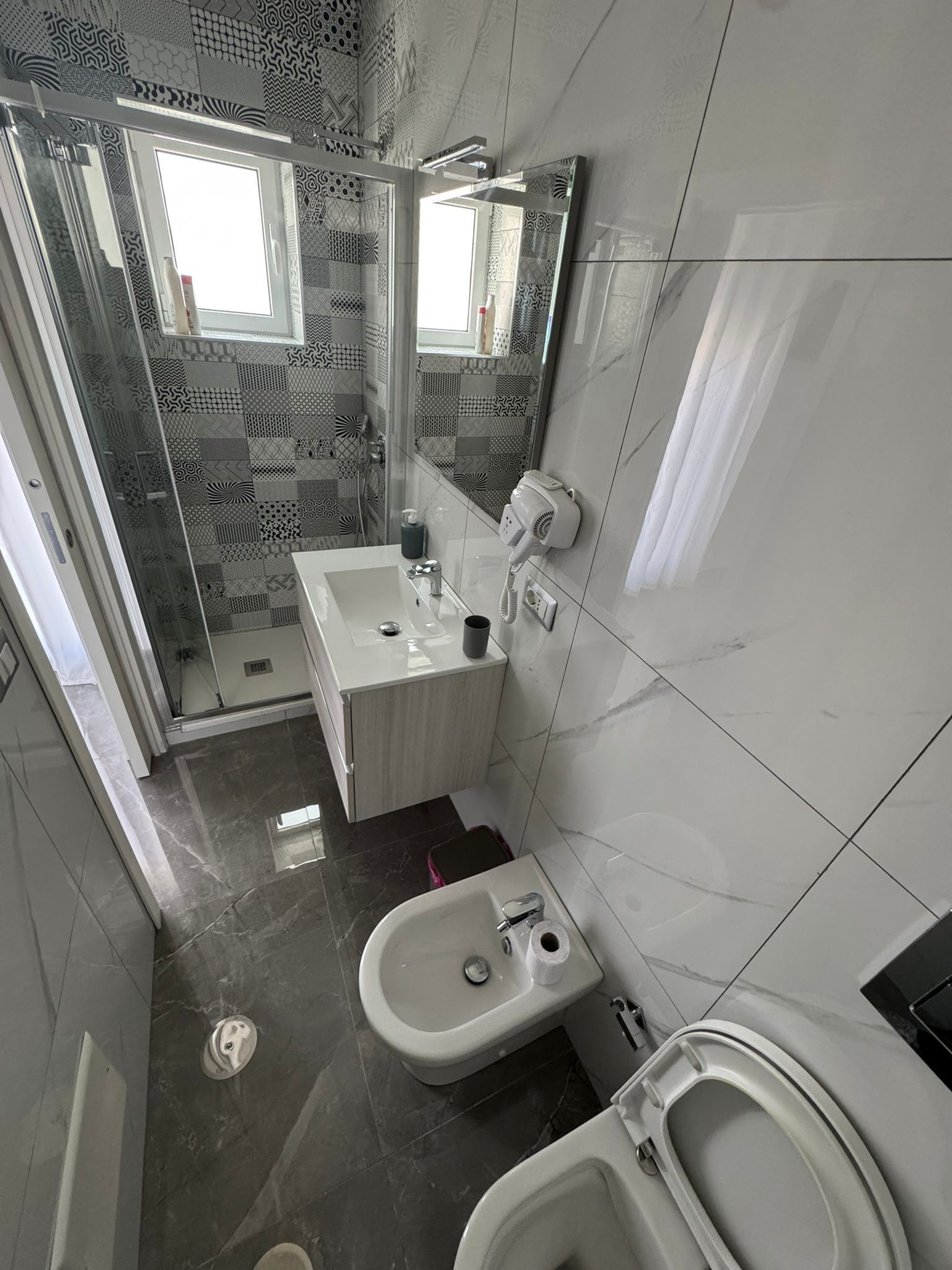 A modern bathroom with a glass shower enclosure, a white sink, a toilet, and a handheld showerhead.