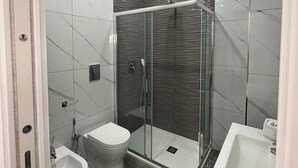 A modern bathroom with a glass-enclosed shower, a bidet, and a sink. - Napolitudine (Naples)