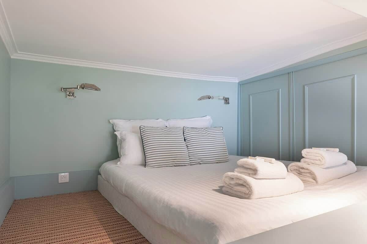 A bedroom with a bed, two wall-mounted light fixtures, and a folded towel on the bed.