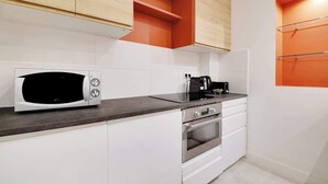 Una cocina compacta con armarios blancos, un microondas, una estufa y una cafetera.