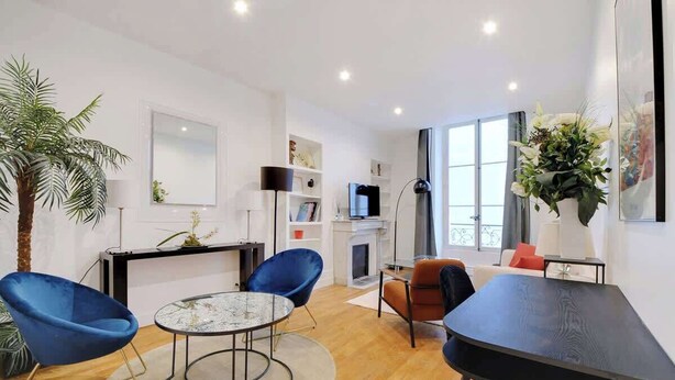 Una sala moderna con una mesa de centro redonda, dos sillones azules, una mesa de comedor negra y una chimenea.