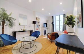 Una sala moderna con una mesa de centro redonda, dos sillones azules, una mesa de comedor negra y una chimenea.