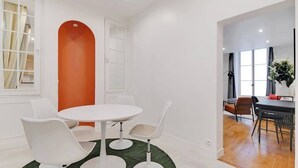 Un comedor moderno con una mesa redonda y sillas blancas, una pared de acento color naranja brillante y vistas a otra habitación con una mesa y sillas para comer.