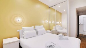 Una habitación de hotel con una cama grande, ropa de cama blanca, una mesita de noche y un espejo.